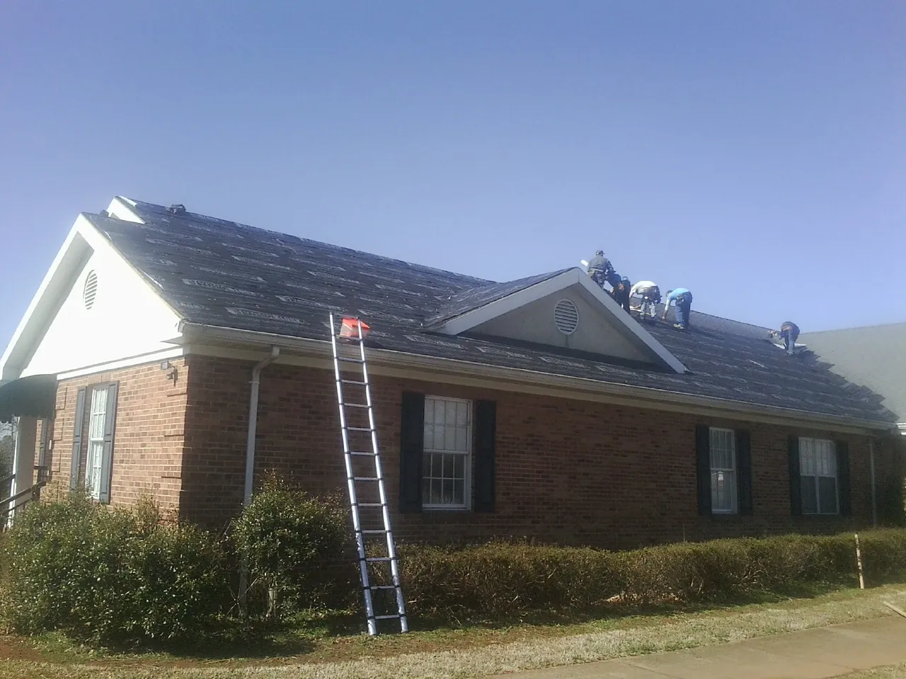 Crew tearing shingles off a brick ranch roof with a ladder set — Emergency Roof Repair work by our crew in Frenchtown
