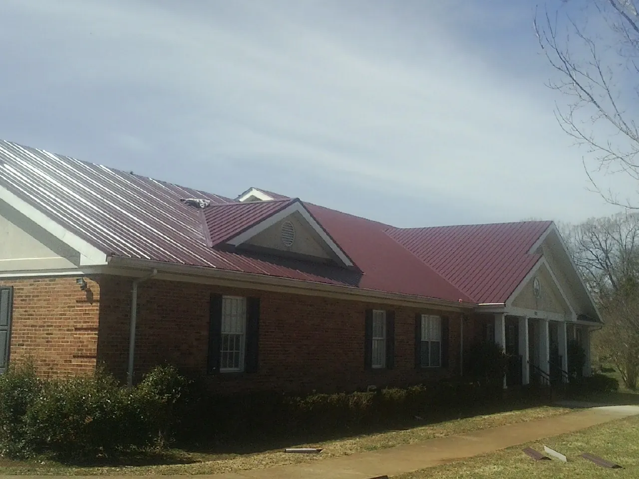 Red metal roof with gabled entries on a long brick building, from a Hail Damage Roof Repair job in Frenchtown