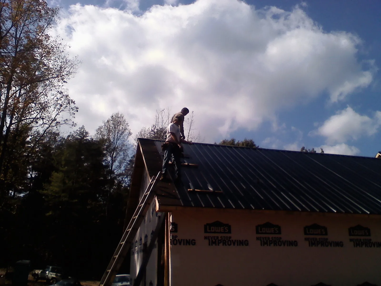 Roofer fastening dark metal panels high against a cloudy sky, from a Roof Inspection job in Frenchtown